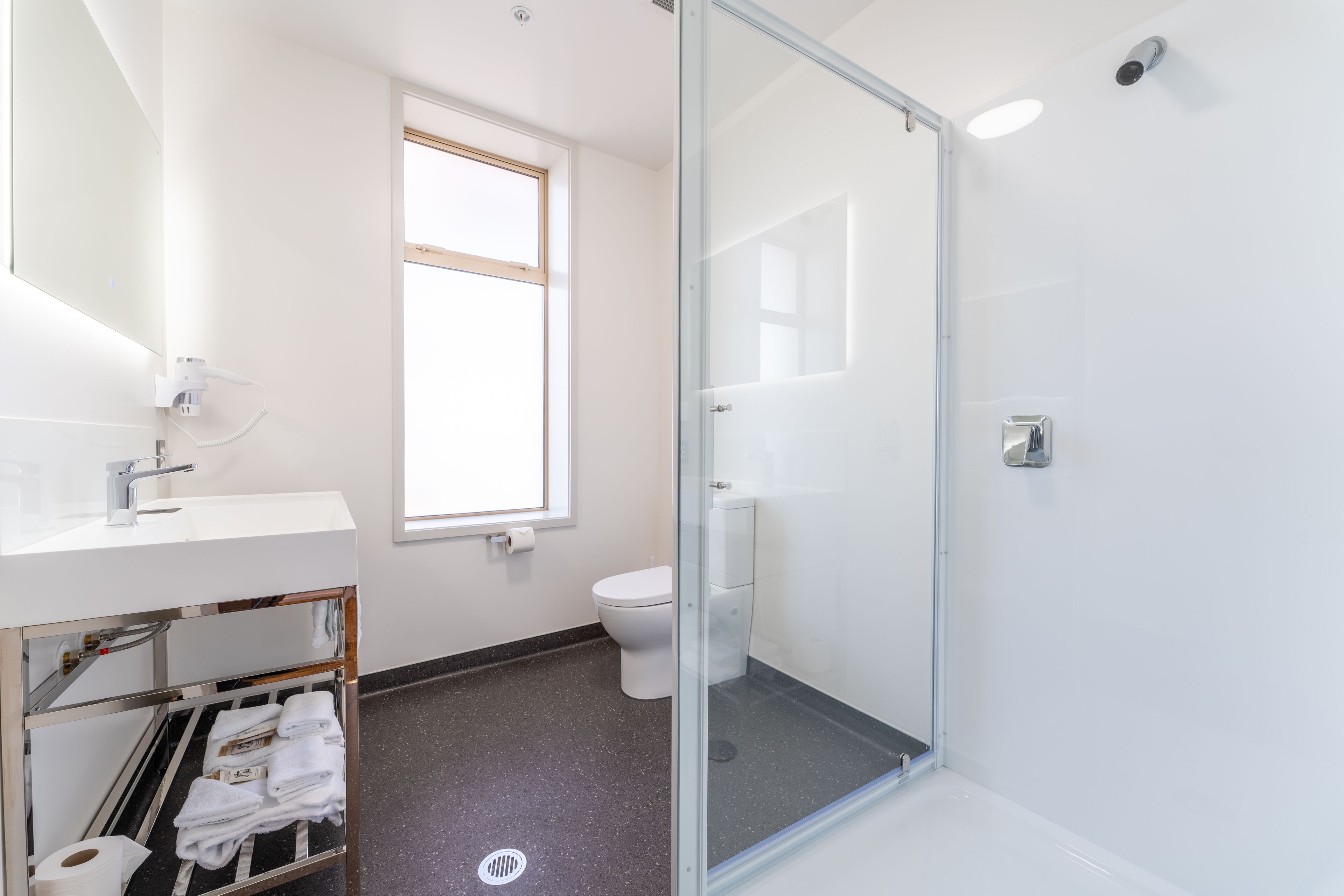 A modern bathroom with a glass shower enclosure, a white toilet, and a sink with a towel rack.