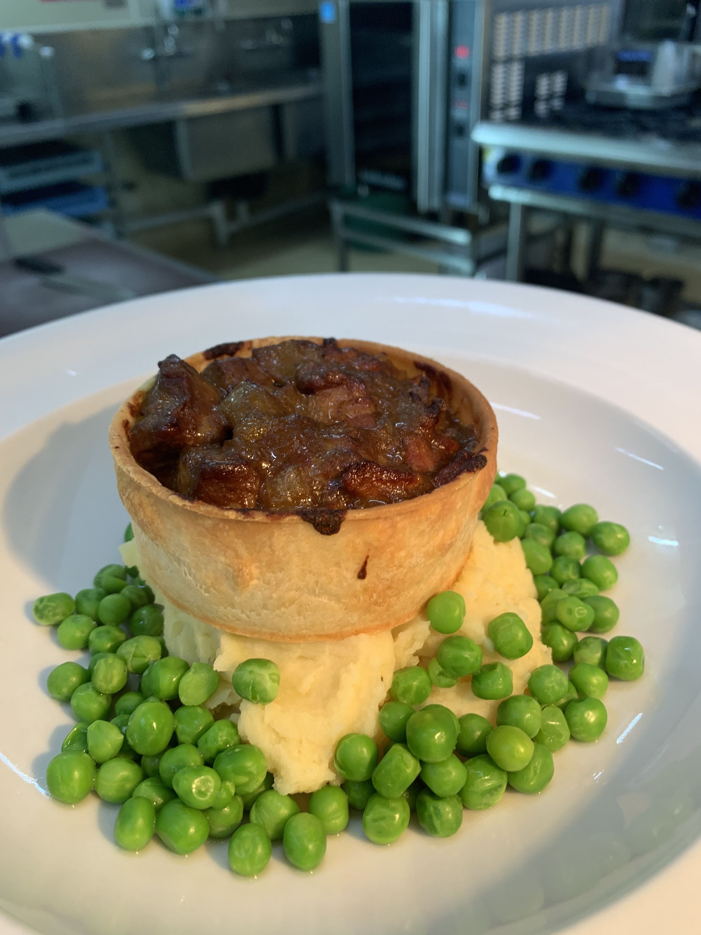 A plate with a meat pie, mashed potatoes, and peas.