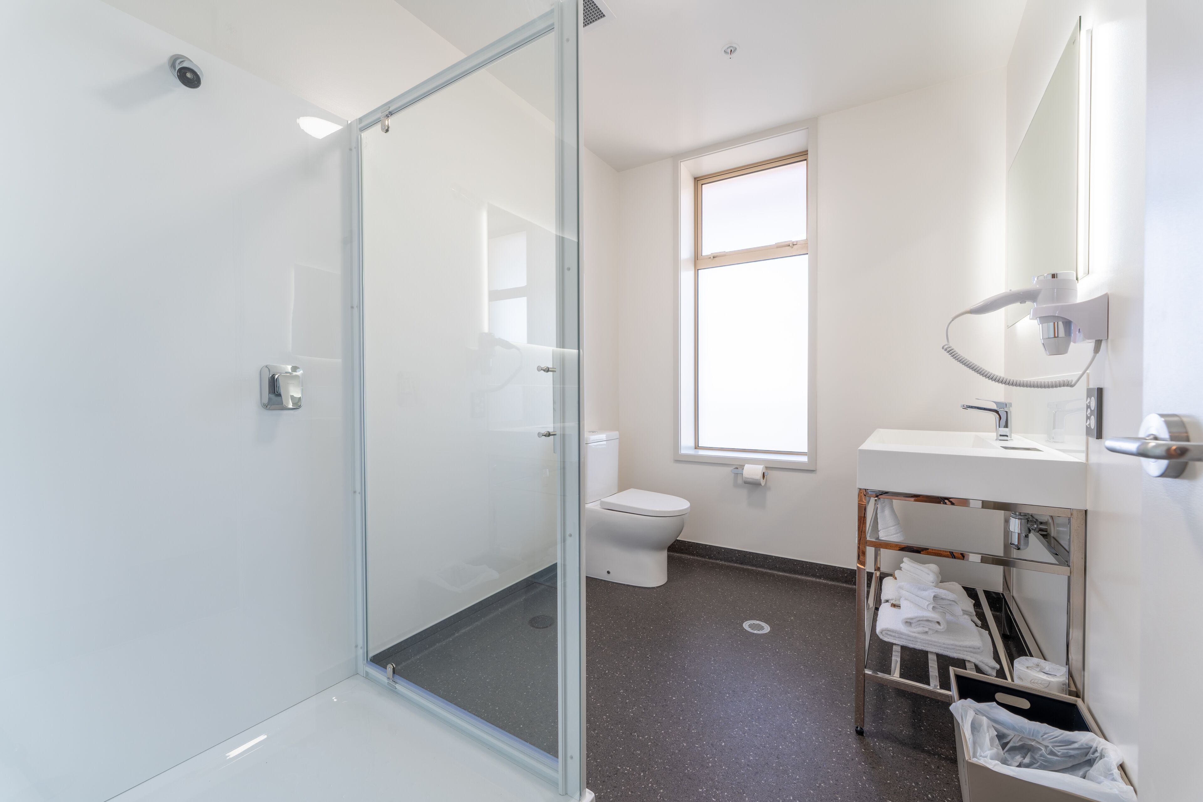 A modern bathroom with a glass shower enclosure, a toilet, a sink with a mirror, and a towel rack.