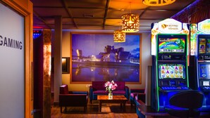 A gaming area with a large screen, comfortable seating, and slot machines. - The Grosvenor (Timaru)