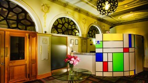 A hotel lobby with wooden doors, a glass table with a vase of flowers, and a colorful wall unit. - The Grosvenor (Timaru)