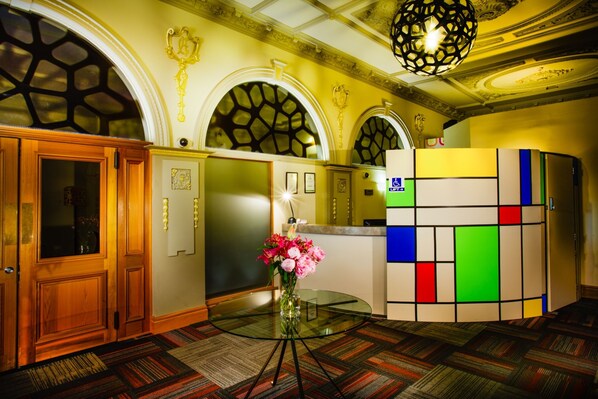 A hotel lobby with wooden doors, a glass table with a vase of flowers, and a colorful wall unit.