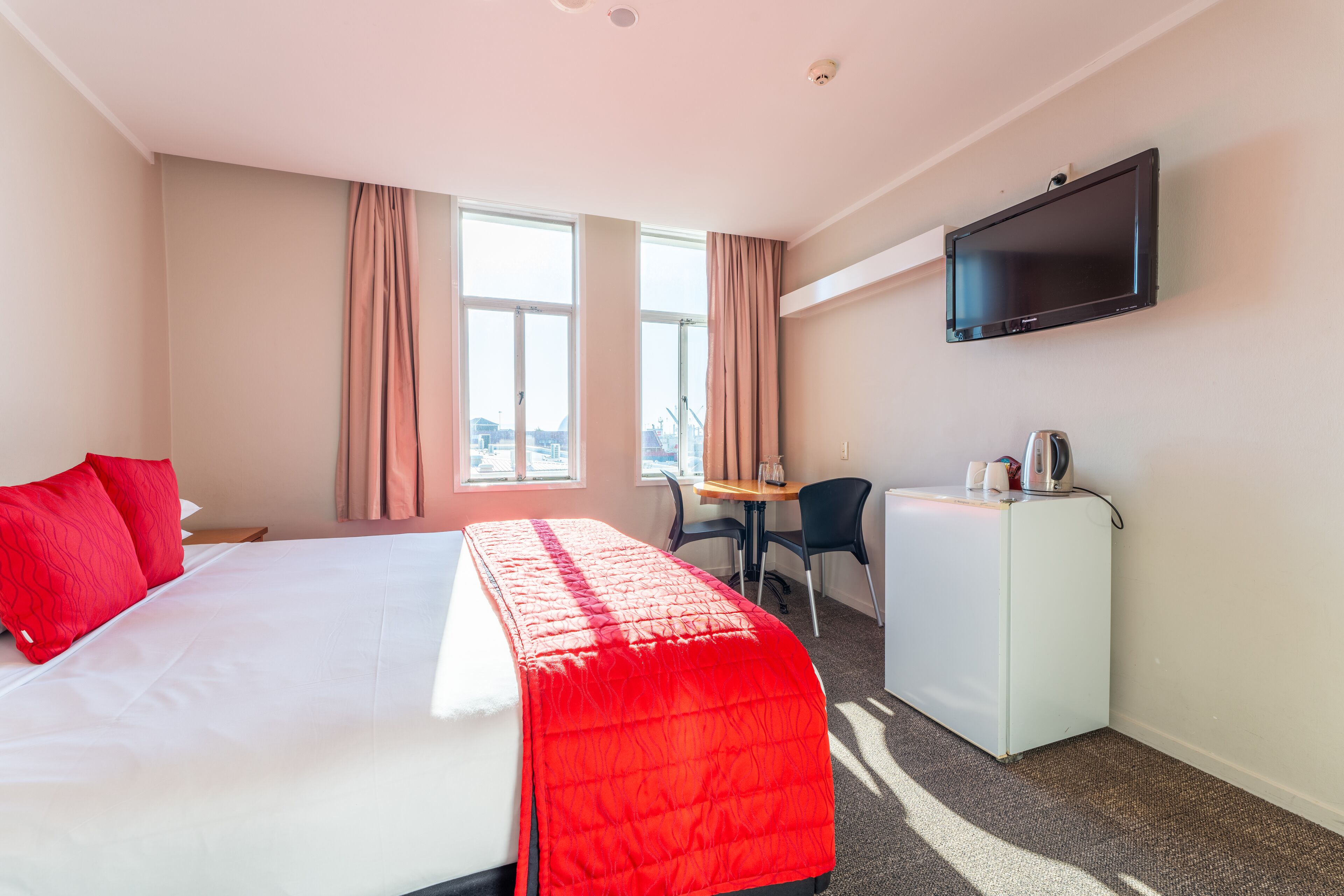 A hotel room with a bed, a desk, a television, and a view of the city.