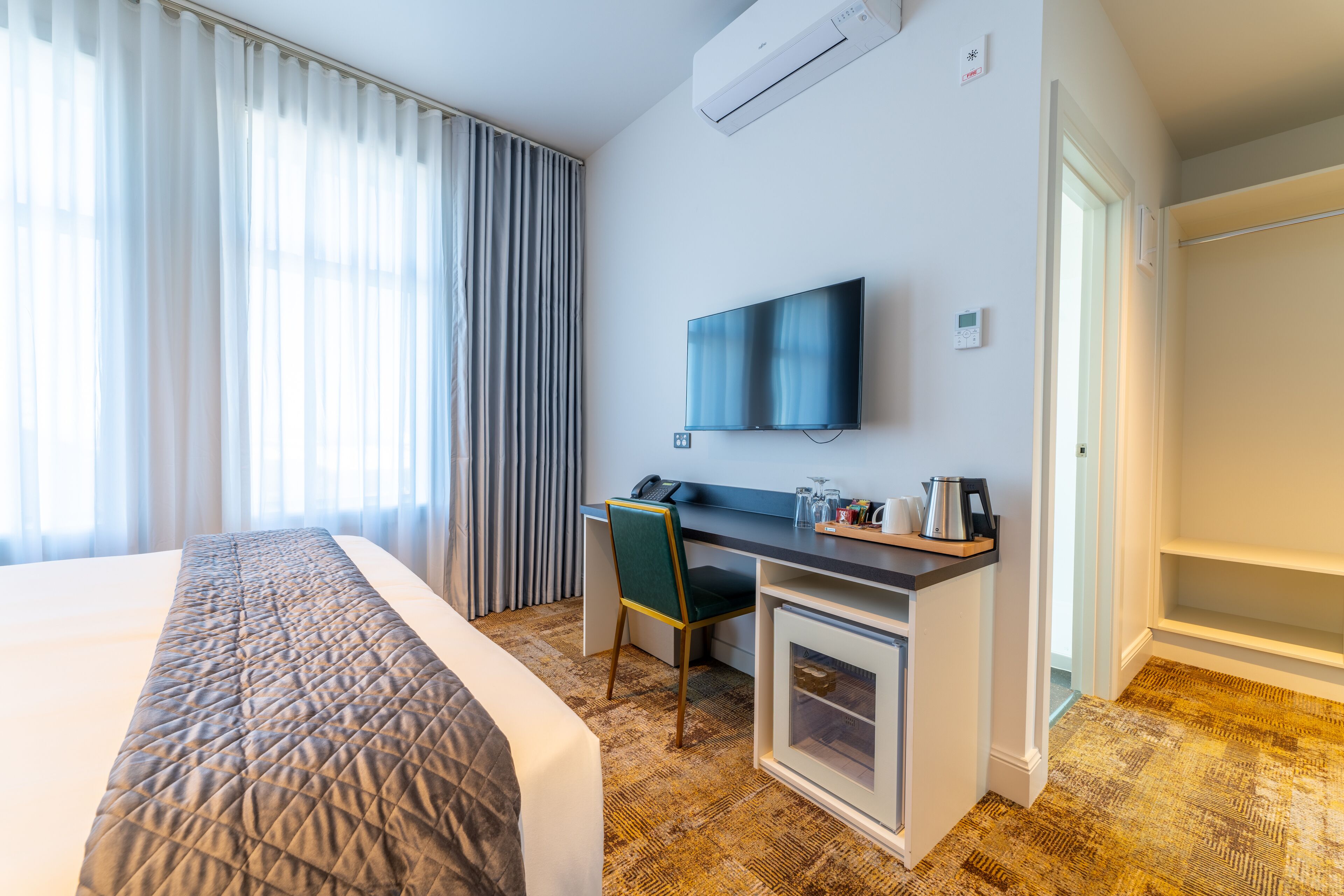 A hotel room with a bed, a desk, a chair, a TV, and a minibar.