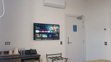 Une chambre d’hôtel dotée d’un téléviseur à écran plat fixé au mur, d’un bureau avec une machine à café, d’un mini-réfrigérateur, d’un étendoir et d’un lit recouvert d’une couette verte.