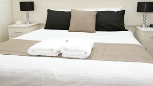 A neatly made bed with a white comforter, two black pillows, and a beige throw blanket. There are two bedside tables with lamps and a phone on one.