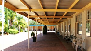 A covered walkway with chairs and tables, palm trees, and a brick pathway. - Renmark Motor Inn Motel (Renmark)