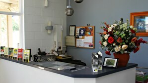 A reception desk with a bulletin board, a framed certificate, a clock, and a vase of flowers. - Renmark Motor Inn Motel (Renmark)