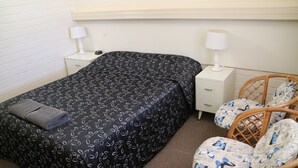 A bedroom with a black bedspread, two bedside tables with lamps, a wicker chair with a butterfly pattern, and a brown carpet.