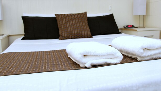 A neatly made bed with white linens, two pillows, and a brown throw blanket.