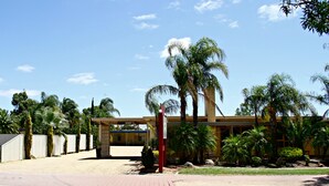 A building with a modern design, featuring a large glass facade and a well-maintained garden with palm trees and shrubs. - Renmark Motor Inn Motel (Renmark)