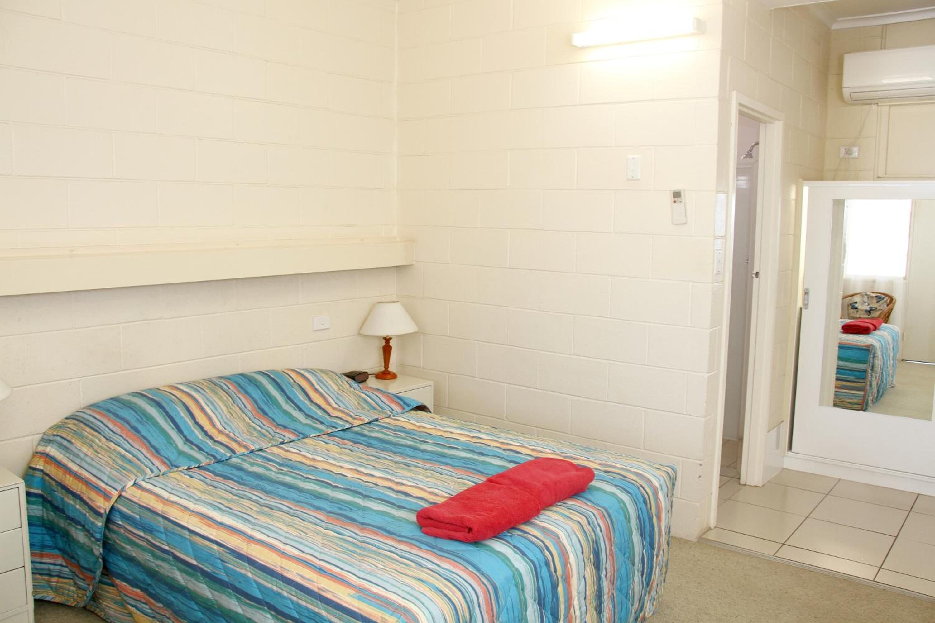 Ett hotellrum med en säng, ett nattduksbord, en lampa och en spegel.