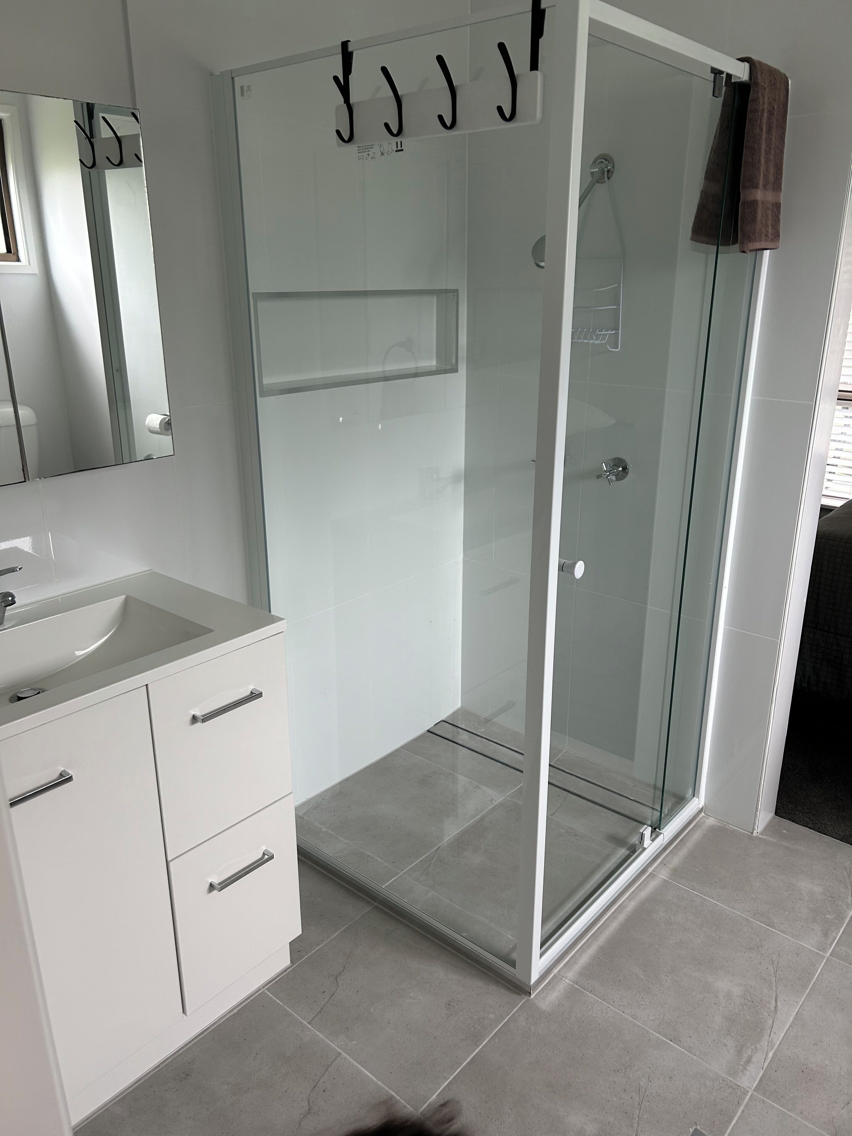 A modern bathroom with a glass-enclosed shower, a white sink, and a mirror.