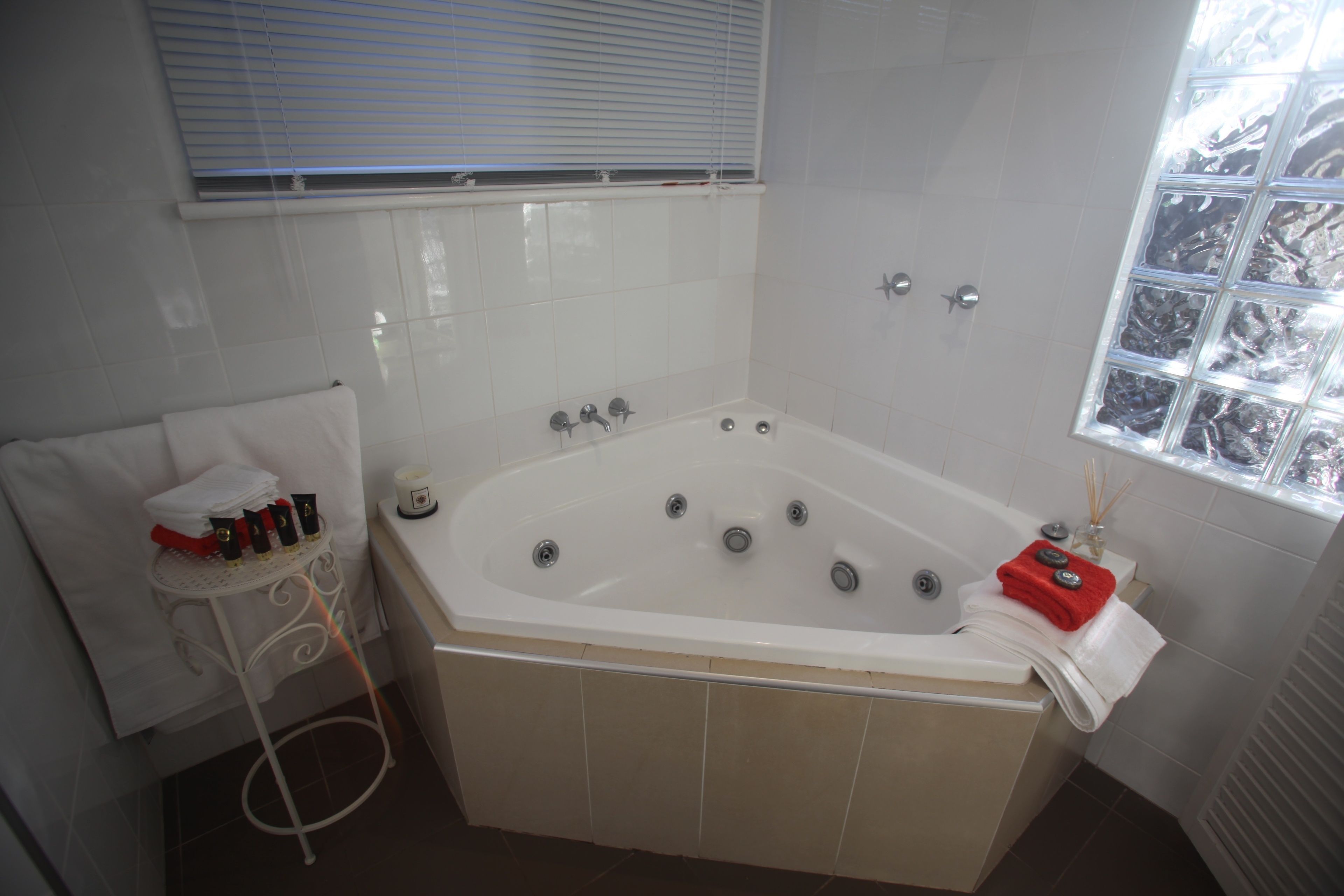 Um banheiro com uma banheira grande, uma janela com persianas e um porta-toalhas com toalhas e produtos de higiene.