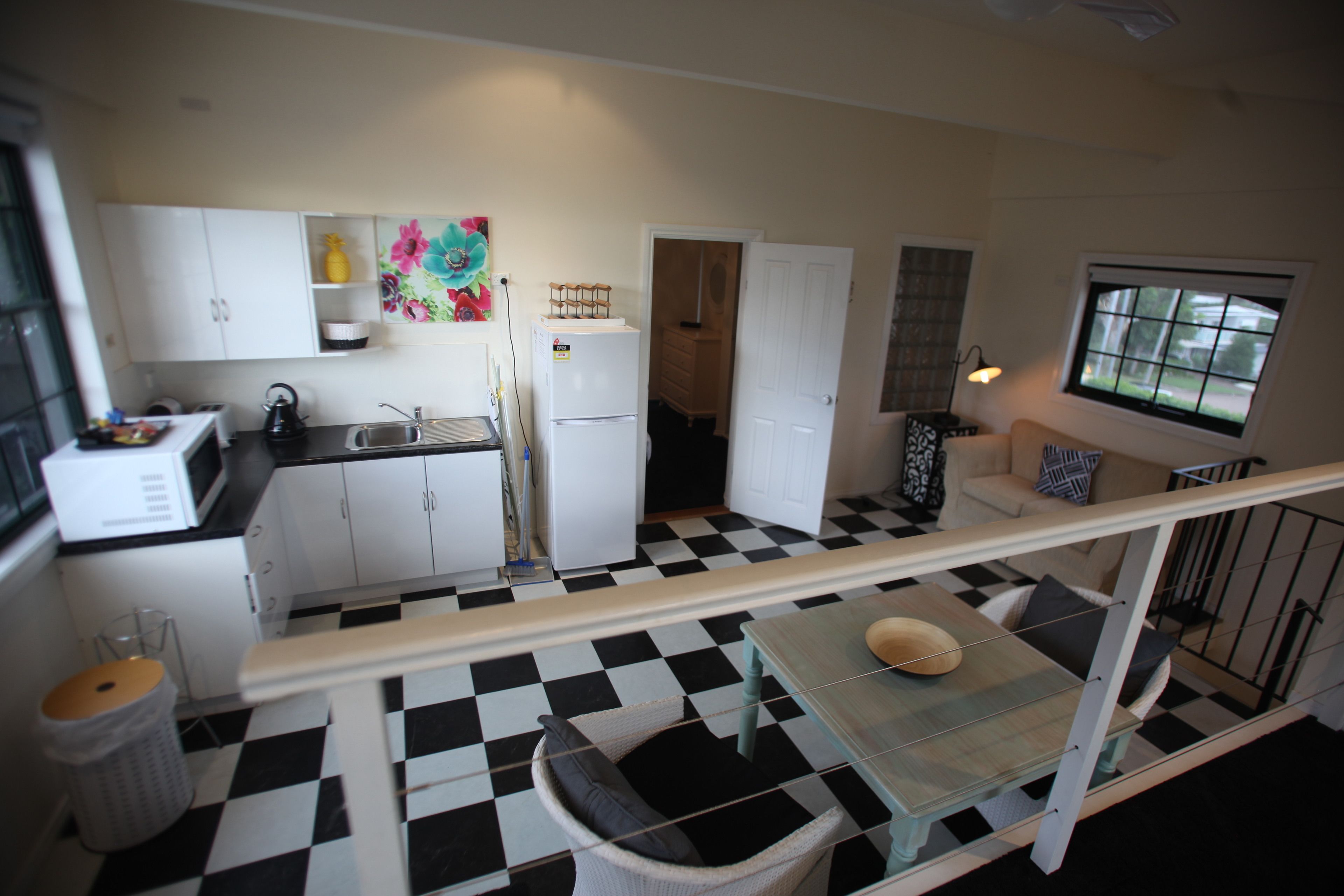 A compact kitchen with white cabinets, a checkered floor, and a dining area with a glass table.