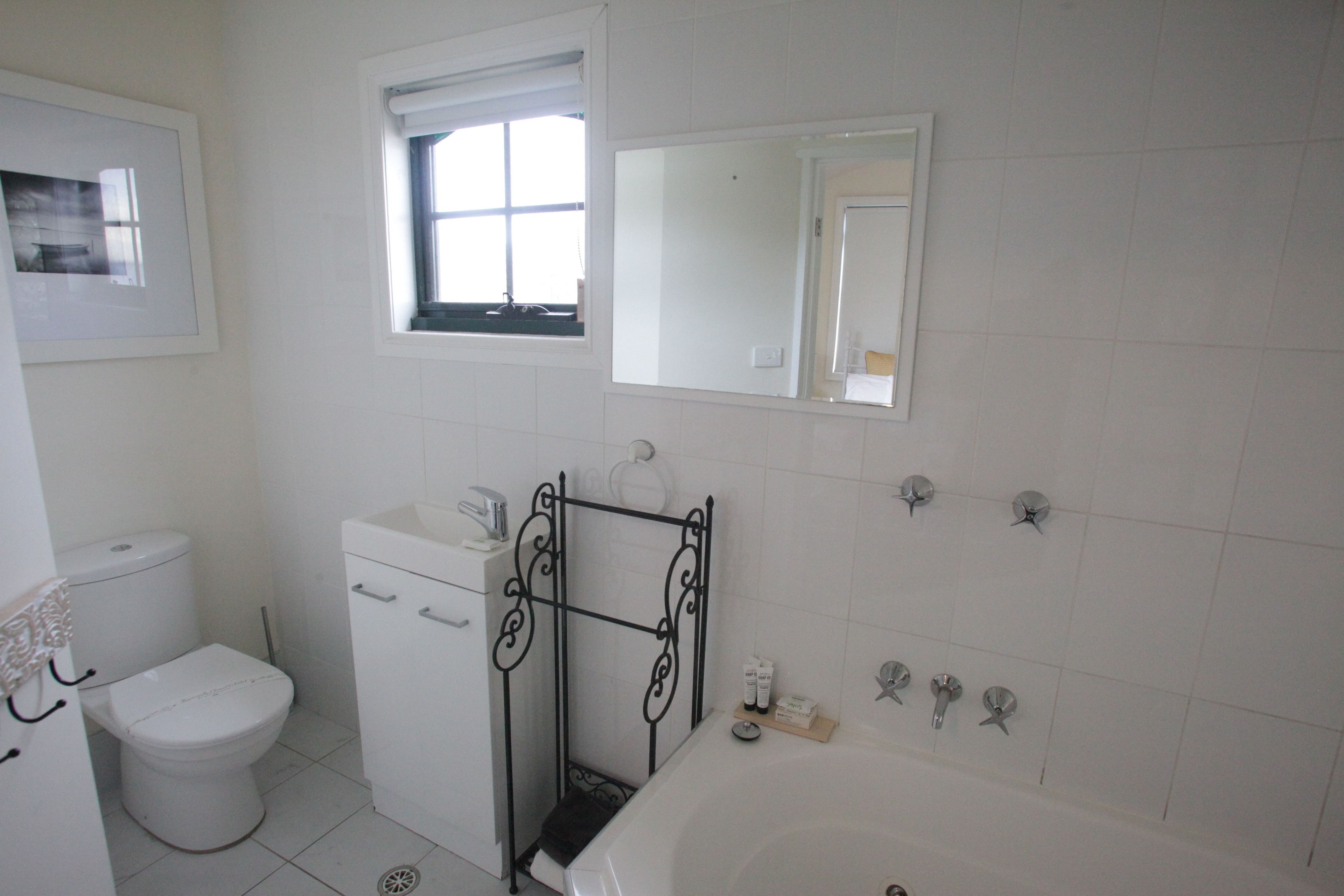 Et badeværelse med toilet, vask, badekar og et vindue.