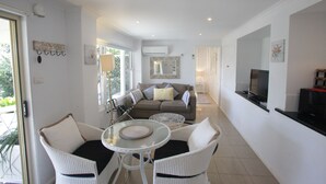 Ein modernes Wohnzimmer mit einer Couch, Sesseln, einem Fernseher und einem Esstisch.