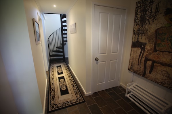 A hallway with a patterned rug, a white door, and a staircase with black railings. - Amore At The Beach (Nelson Bay)