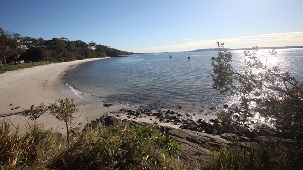 Ein Strand mit klarem Wasser, sandigem Ufer und einigen Felsen.