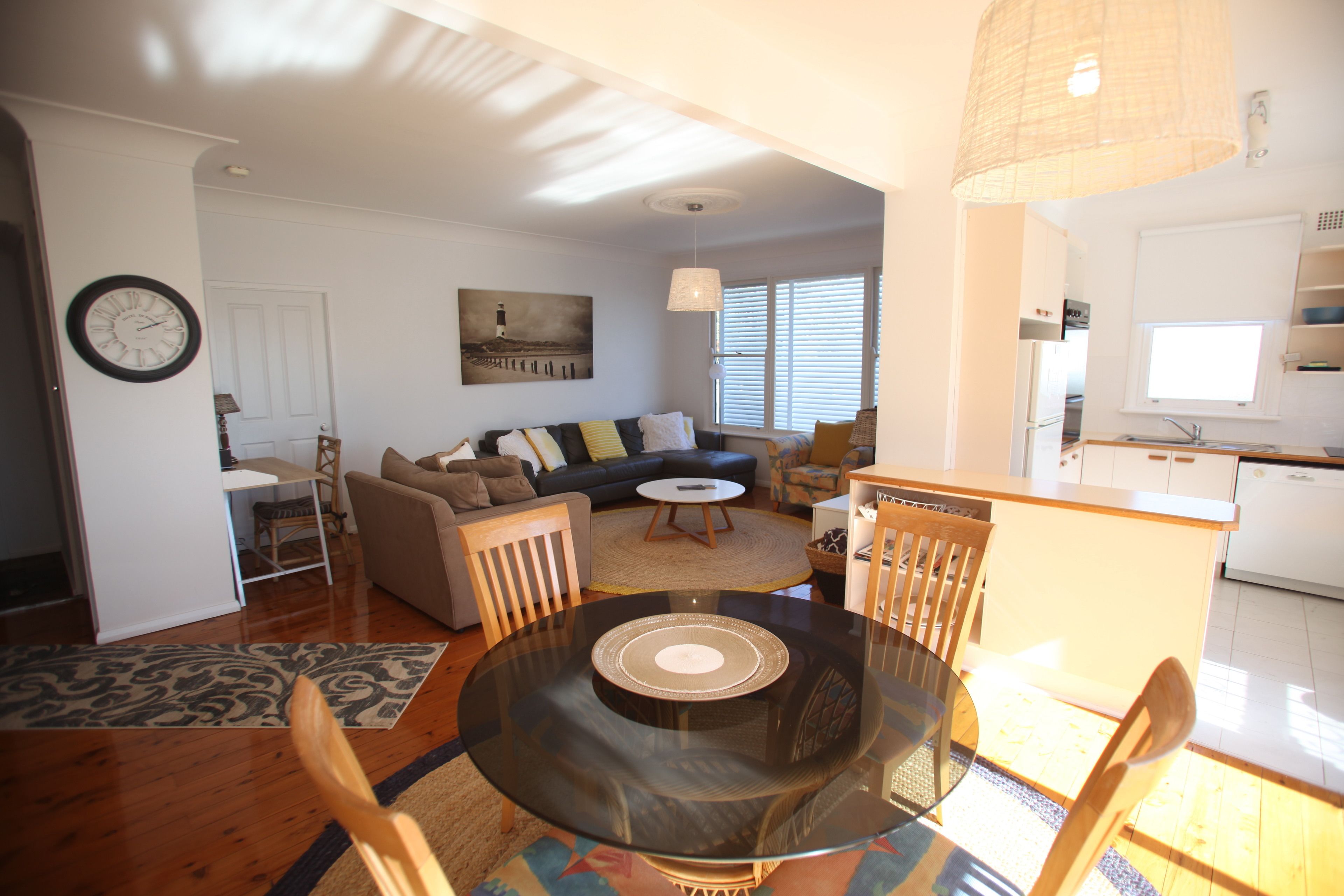 A modern living room with a glass coffee table, a sofa, and a dining area with chairs.