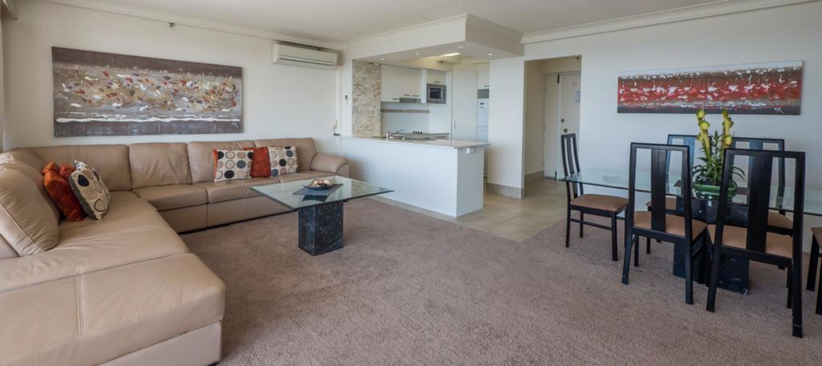 A living room with a beige sofa, a glass coffee table, and a dining area with a glass table and chairs.