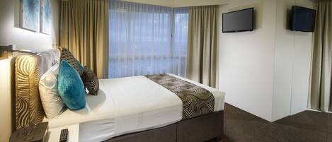 A hotel room with a bed, a TV, and a window with curtains.