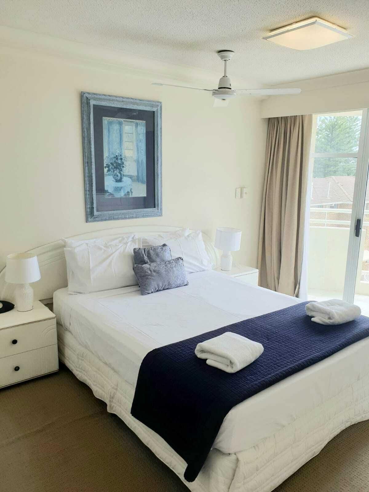 Habitación de hotel con una cama grande, ventilador de techo, un cuadro enmarcado en la pared y una ventana con cortinas.