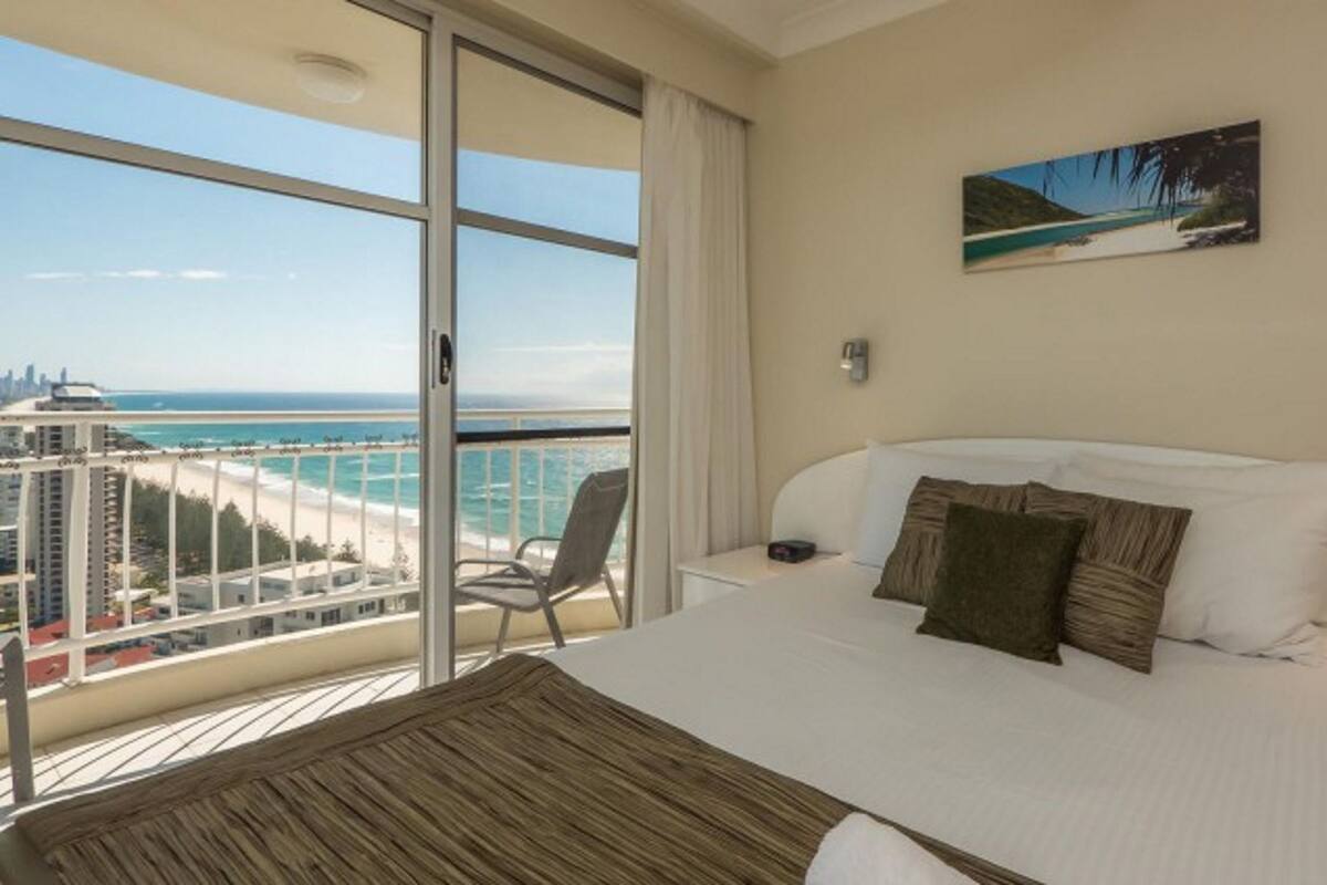 Une chambre d’hôtel avec un grand lit, une vue sur la plage et le paysage urbain, et un tableau accroché au mur.