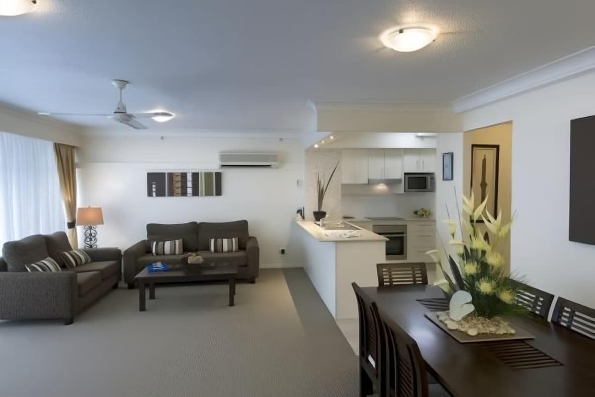 A modern living room with a sofa set, a coffee table, and a dining table with chairs. There is a kitchen area with cabinets and a microwave.