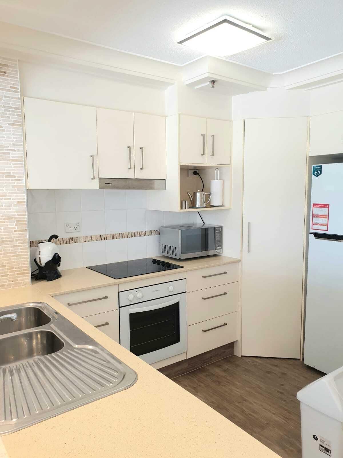 A modern kitchen with white cabinets, a built-in microwave, a stove, and a sink.