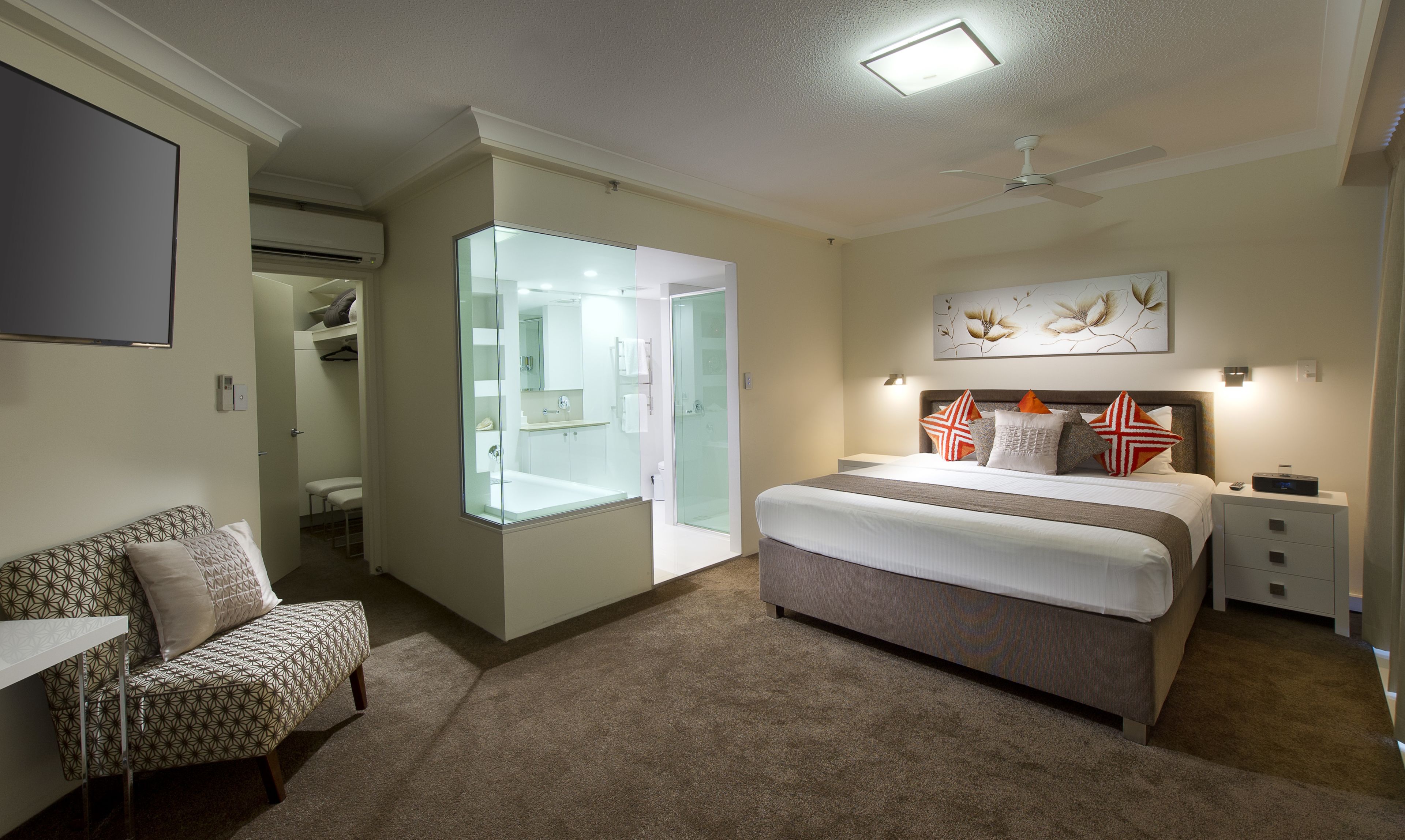 Un dormitorio moderno con una cama grande, una mesita de noche, una silla, cabina de ducha con paredes de vidrio y un ventilador de techo.