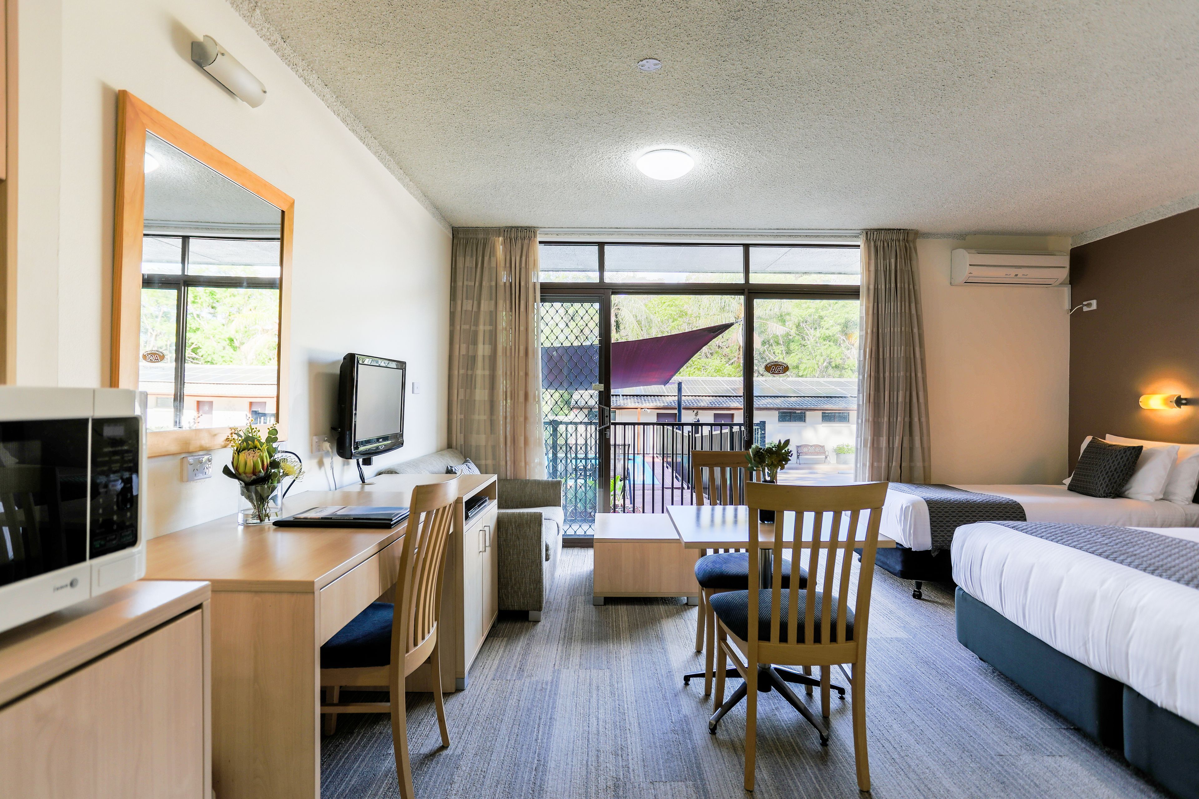A hotel room with a desk, chair, bed, and a balcony with a view.