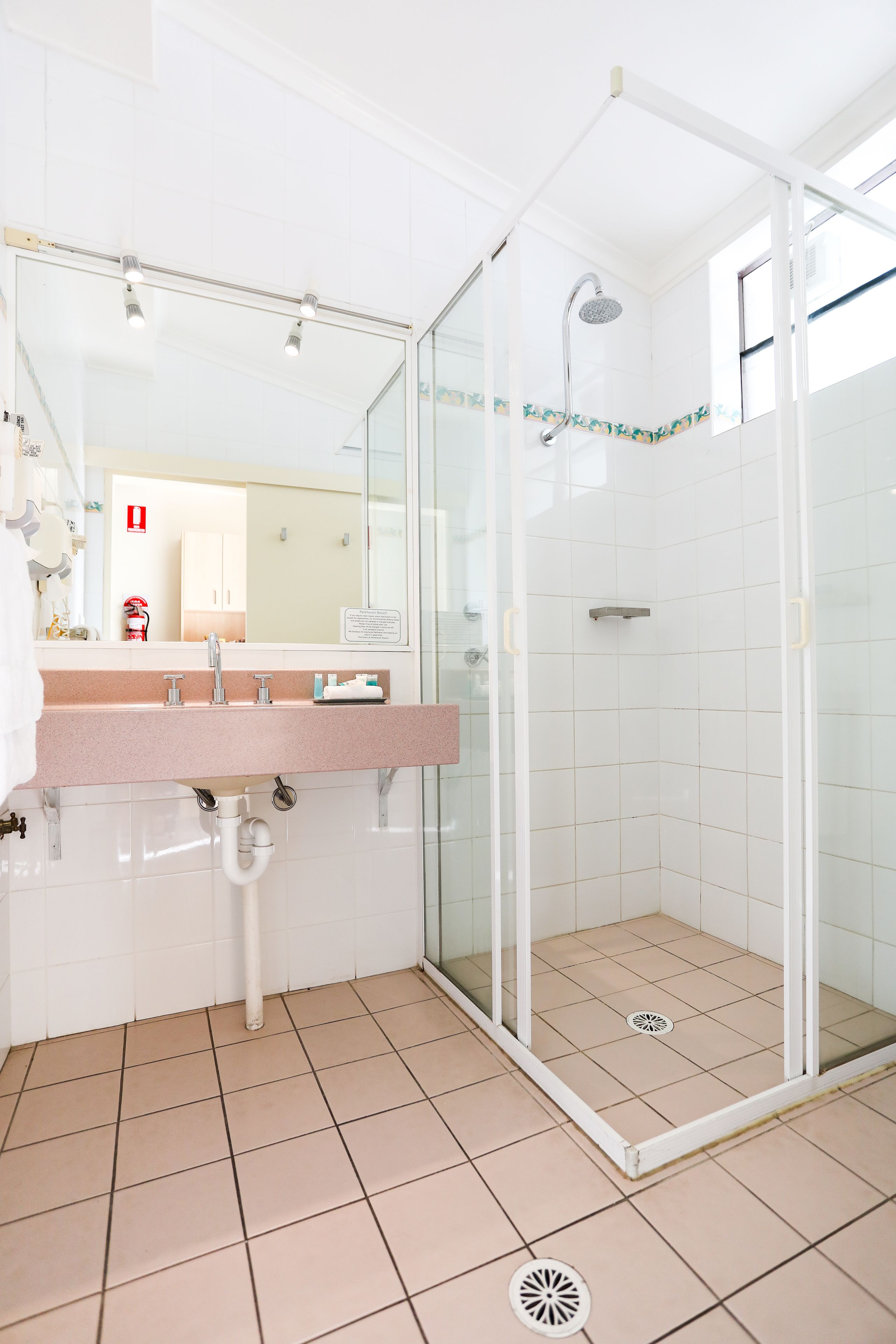 A bathroom with a glass-enclosed shower, a sink with a mirror, and a tiled floor.