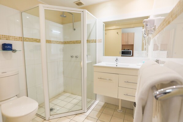 Un baño con ducha envuelta en vidrio, un lavabo blanco y un espejo sobre él.