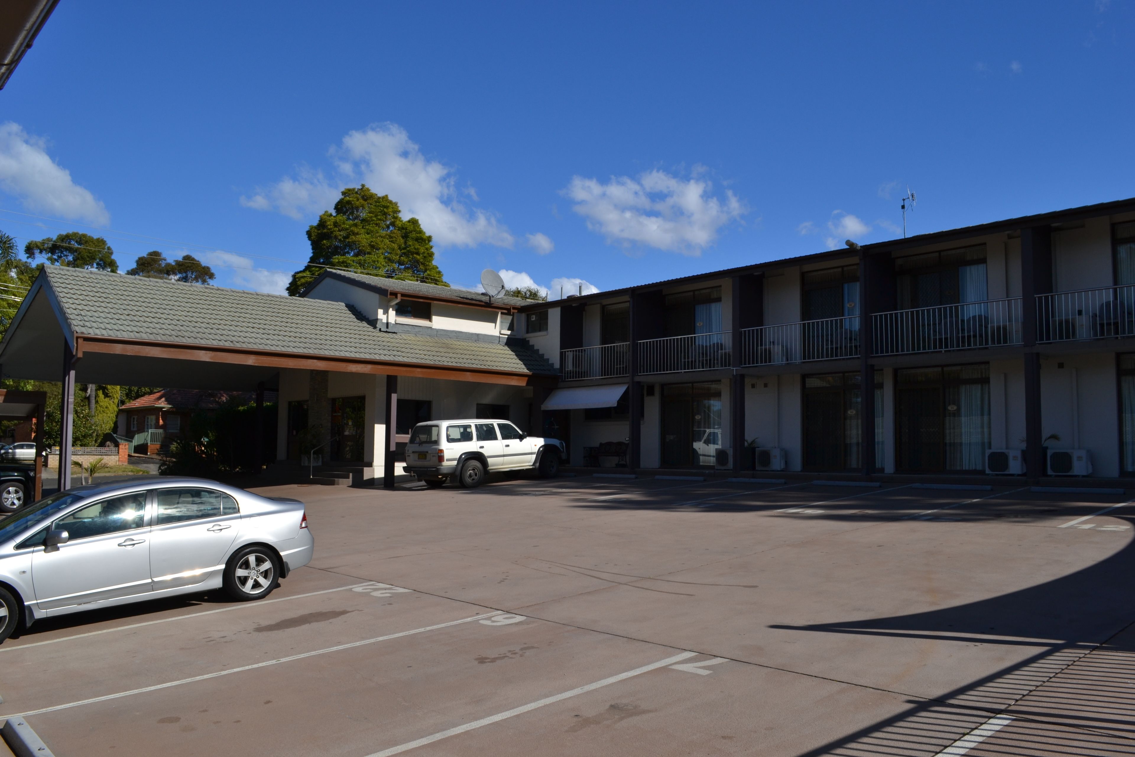 A motel with a covered parking area, a white car, and a building with balconies.