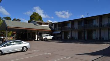 A motel with a covered parking area, a white car, and a building with balconies.