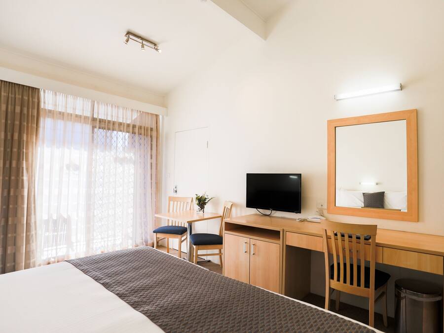 Ein Hotelzimmer mit Bett, Schreibtisch, Stuhl, Fernseher und einem großen Fenster mit Vorhängen.