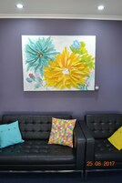 A room with a purple wall, a large floral painting, and two black leather sofas with colorful pillows.