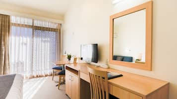 Une chambre d’hôtel équipée d’un lit, d’un bureau, d’une chaise, d’une télévision et d’un grand miroir.