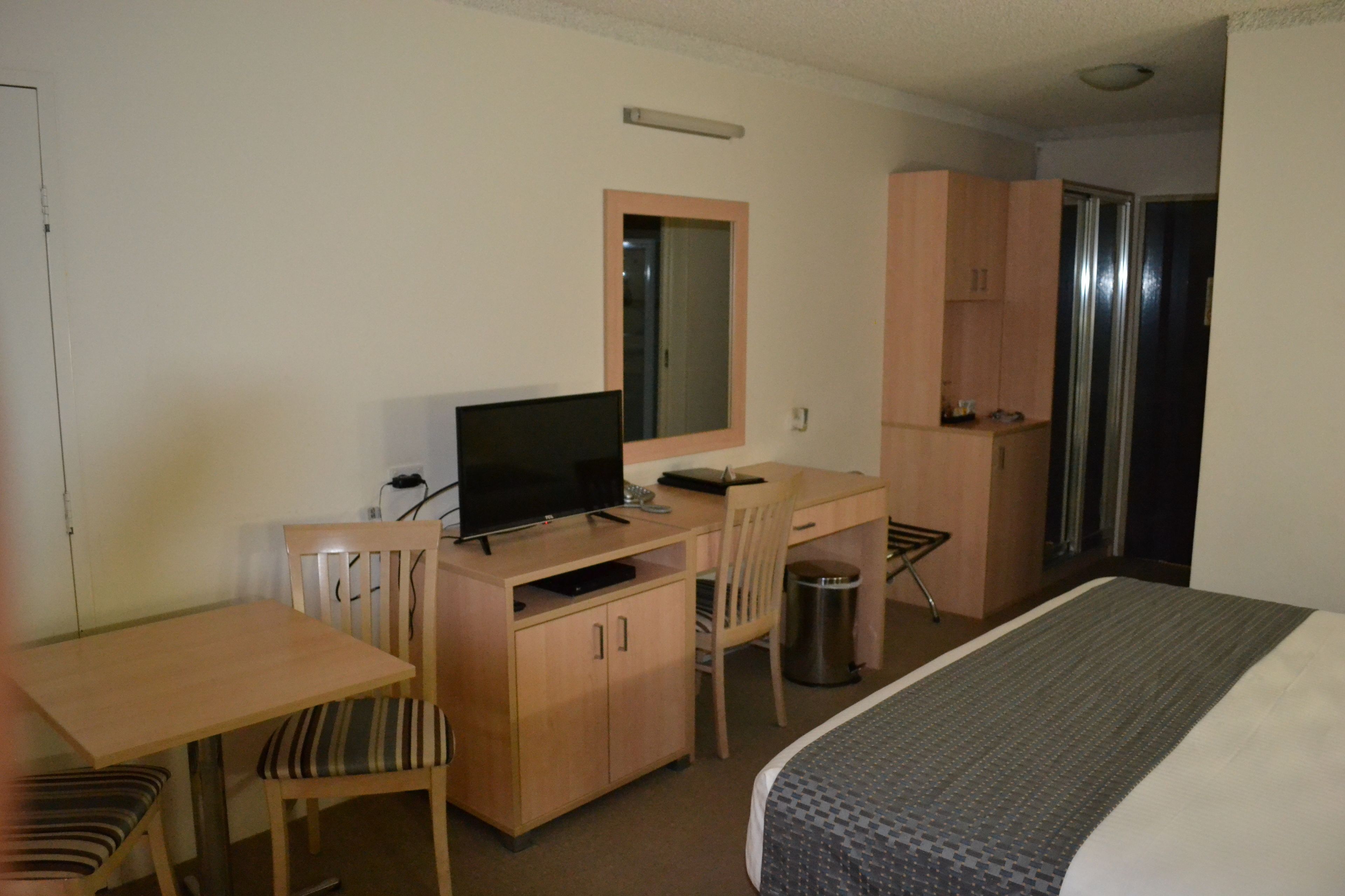 Quarto de hotel com uma cama, escrivaninha com computador, uma cadeira, televisão e um pequeno cesto de lixo.