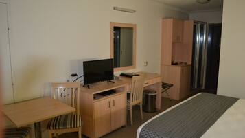Quarto de hotel com uma cama, escrivaninha com computador, uma cadeira, televisão e um pequeno cesto de lixo.