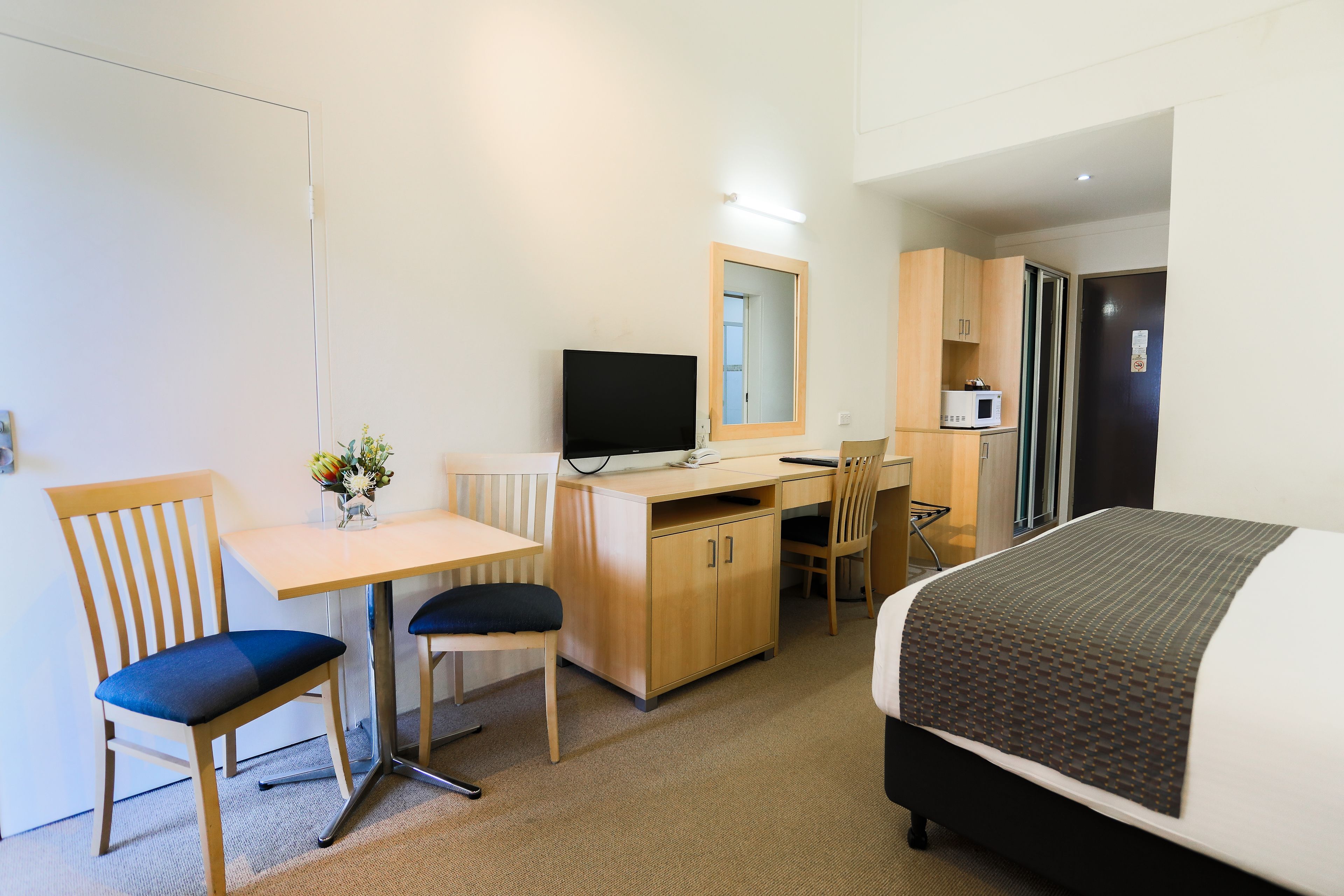 A hotel room with a bed, a desk with a chair, a television, a microwave, and a small cabinet.