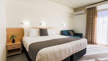 A neatly arranged hotel room with a large bed, bedside tables, a small seating area, and an air conditioning unit.
