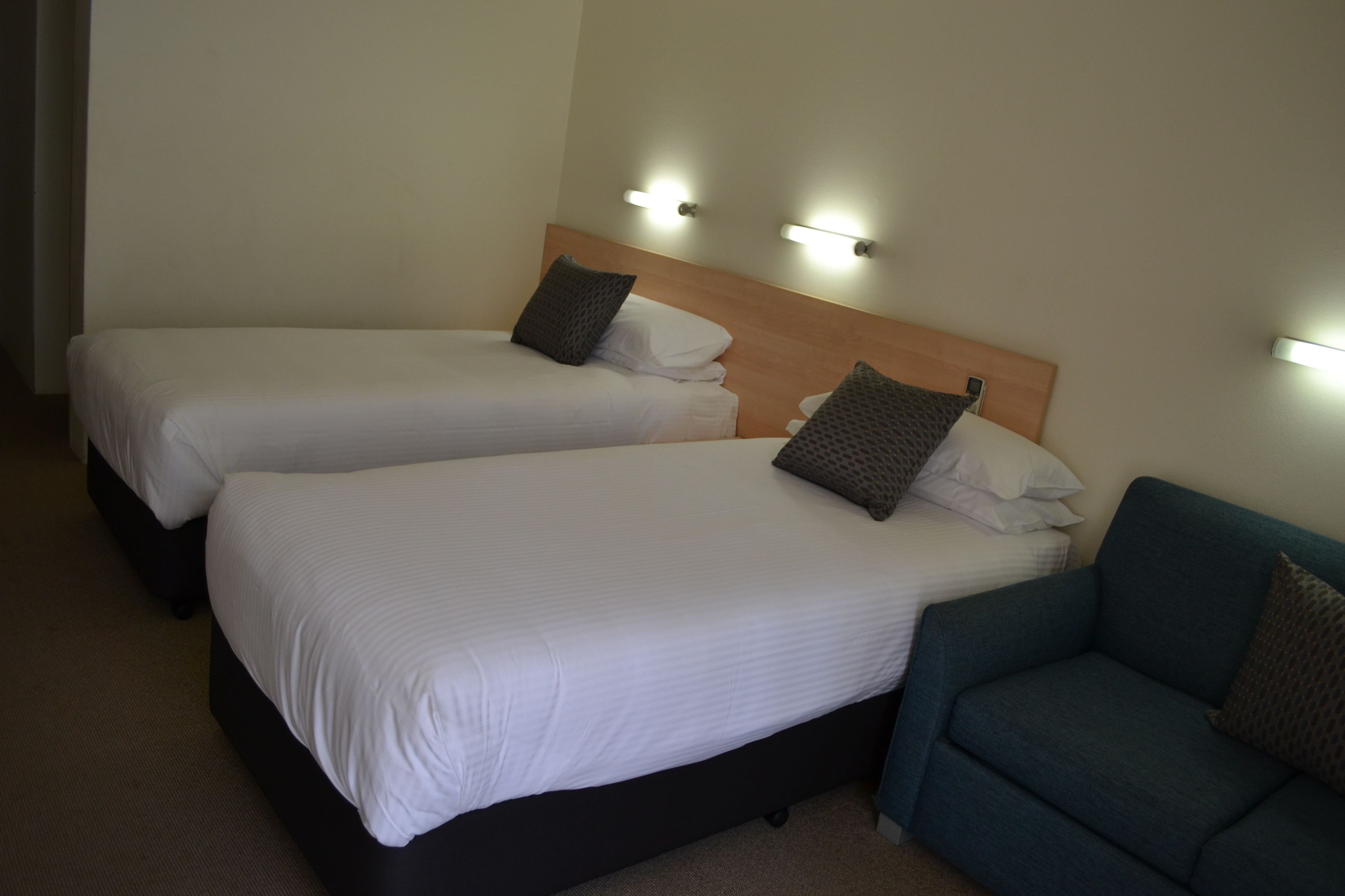Two single beds with headboards, a blue sofa, and wall-mounted lights.