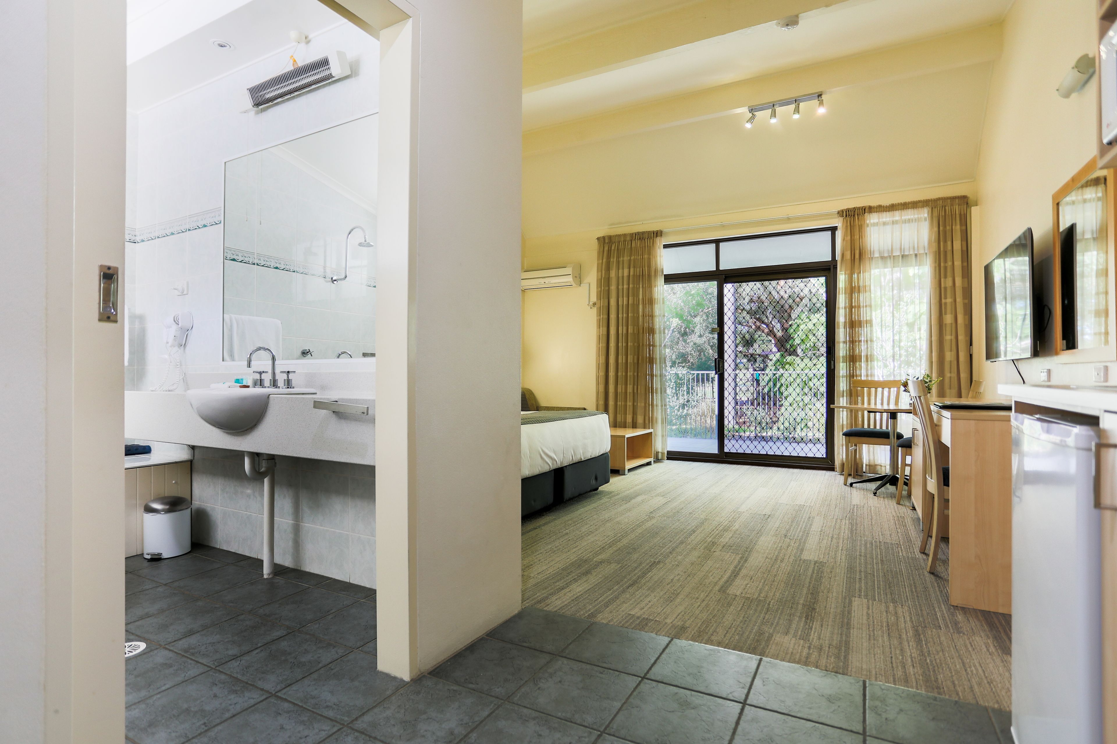 A modern hotel room with a large bathroom, a bed, a desk, and a view of the outdoors.