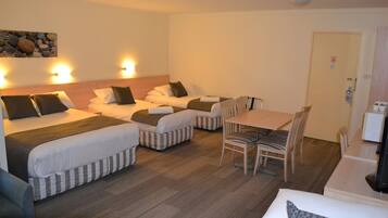 A hotel room with two single beds, a dining table with chairs, and a small kitchenette.