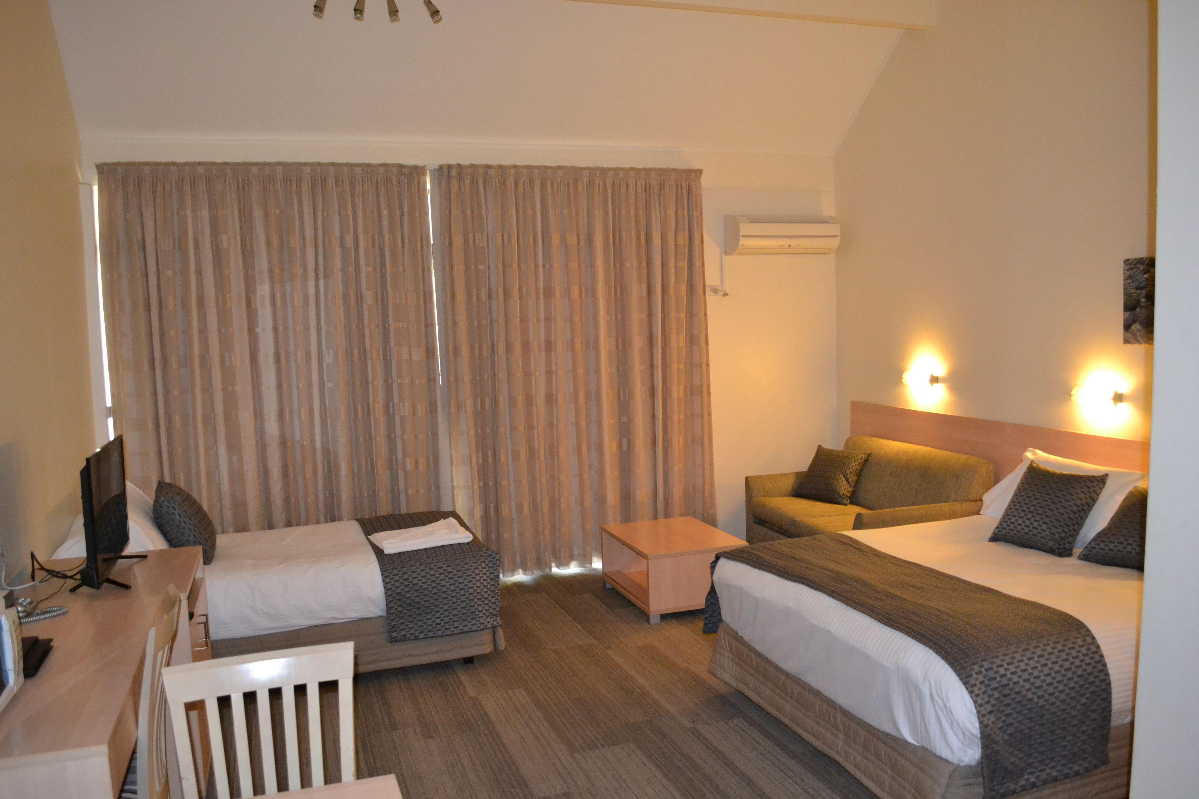 A hotel room with two beds, a desk, a chair, a small table, and a television.