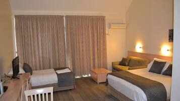 A hotel room with two beds, a desk, a chair, a small table, and a television.