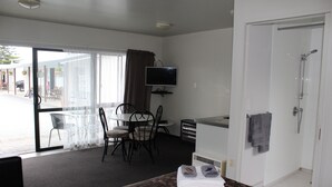A hotel room with a bed, a desk, a chair, a television, and a shower. - Sierra Beachfront Motel (Kaikoura)