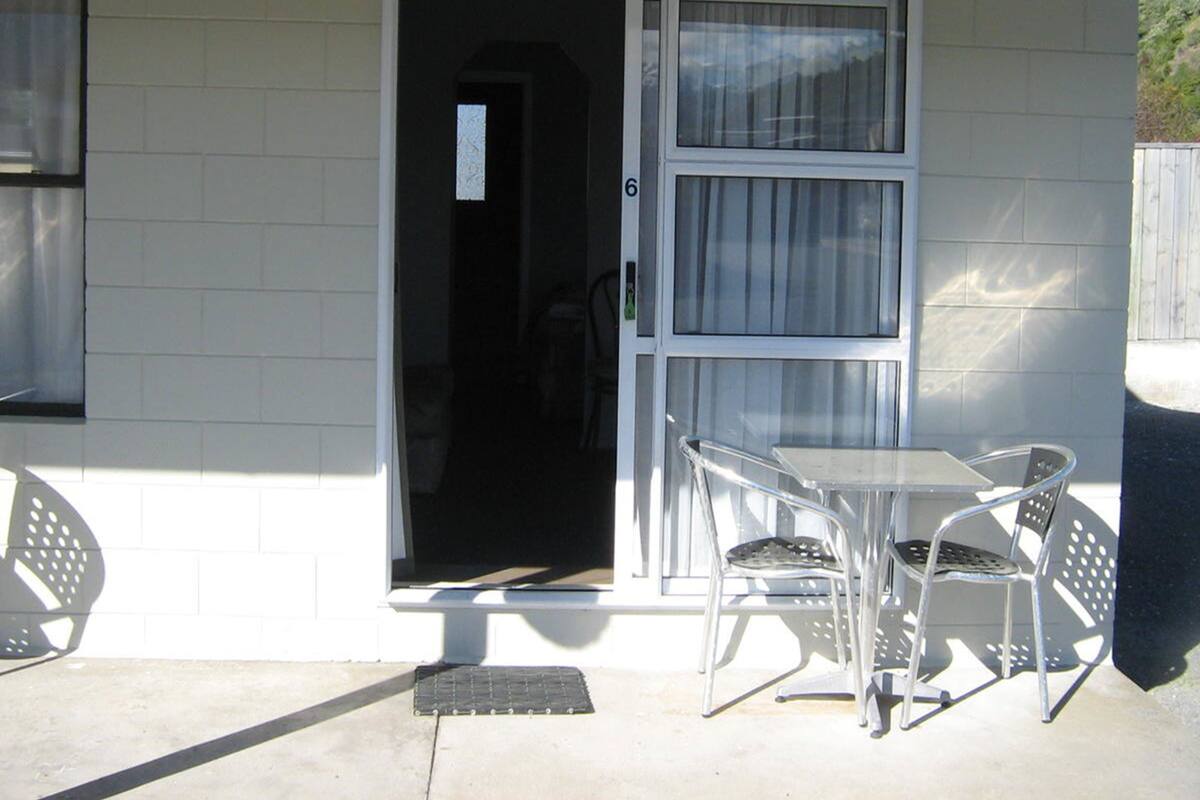 A white building with a door and windows, a small table with chairs, and a metal chair outside.